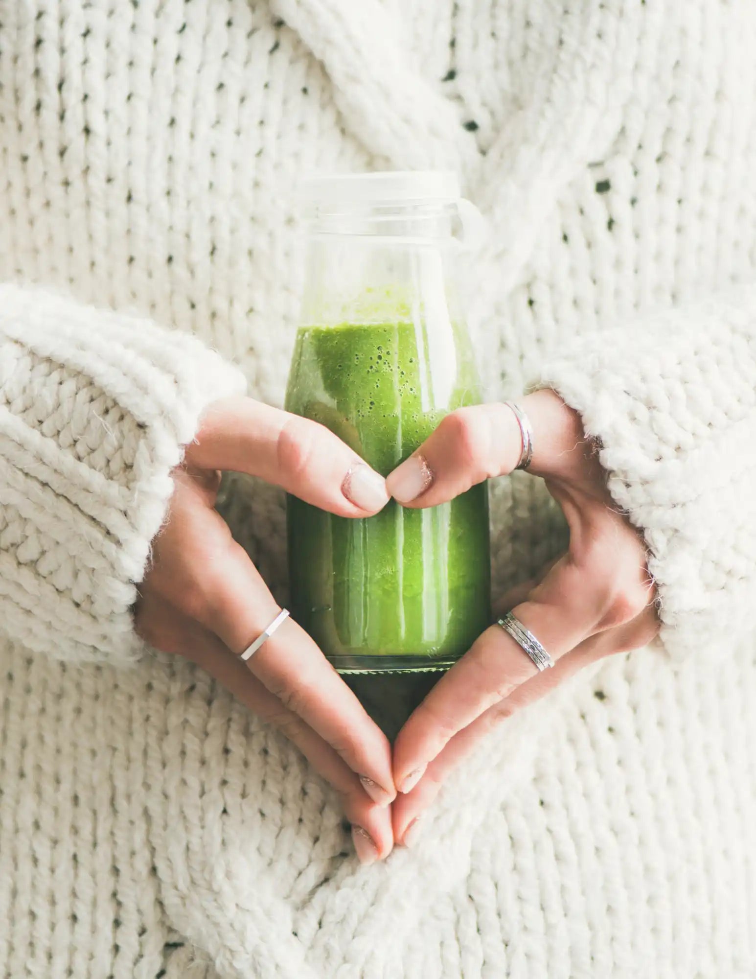 Green smoothie in a glass bottle held in heart-shaped hands.