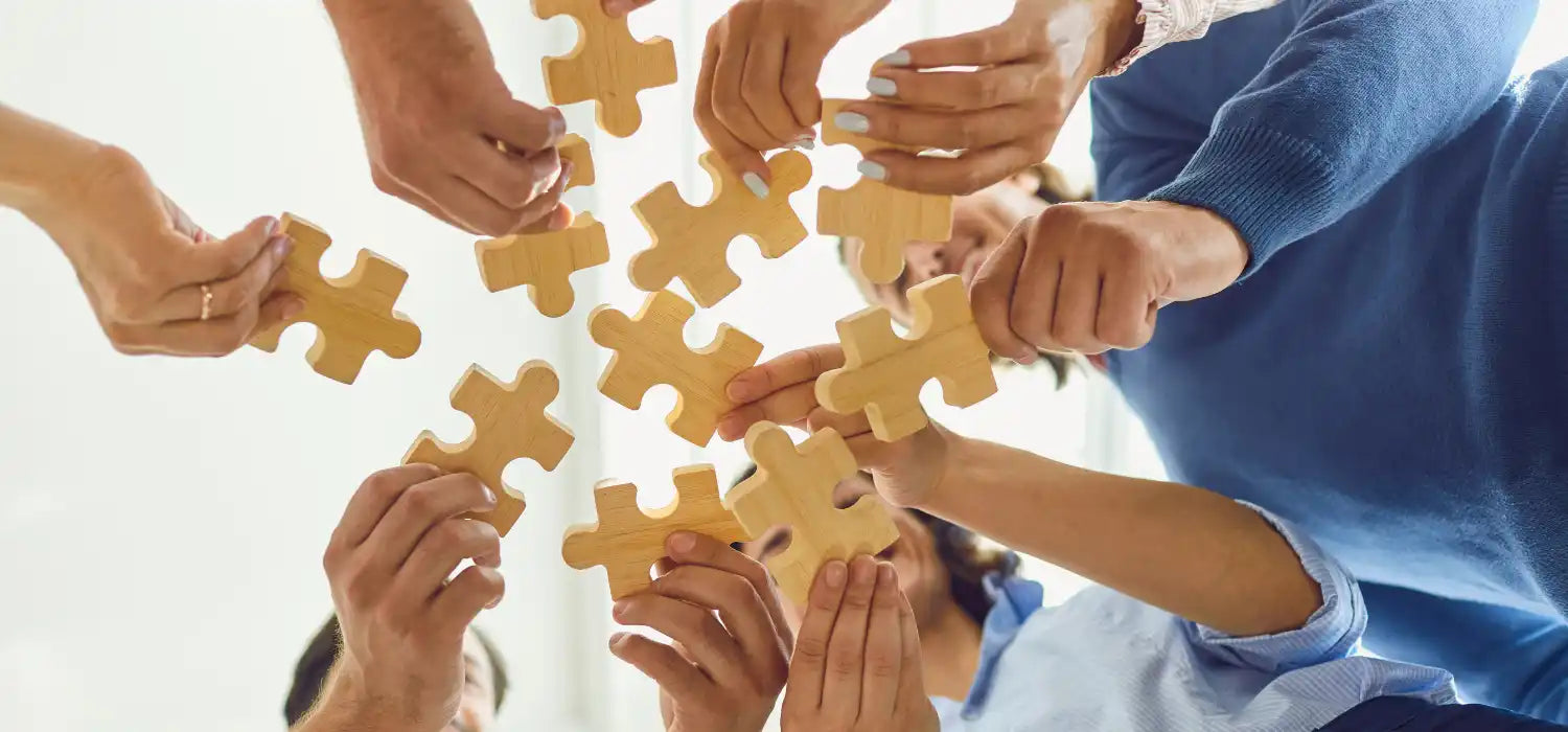Multiple hands holding wooden puzzle pieces.